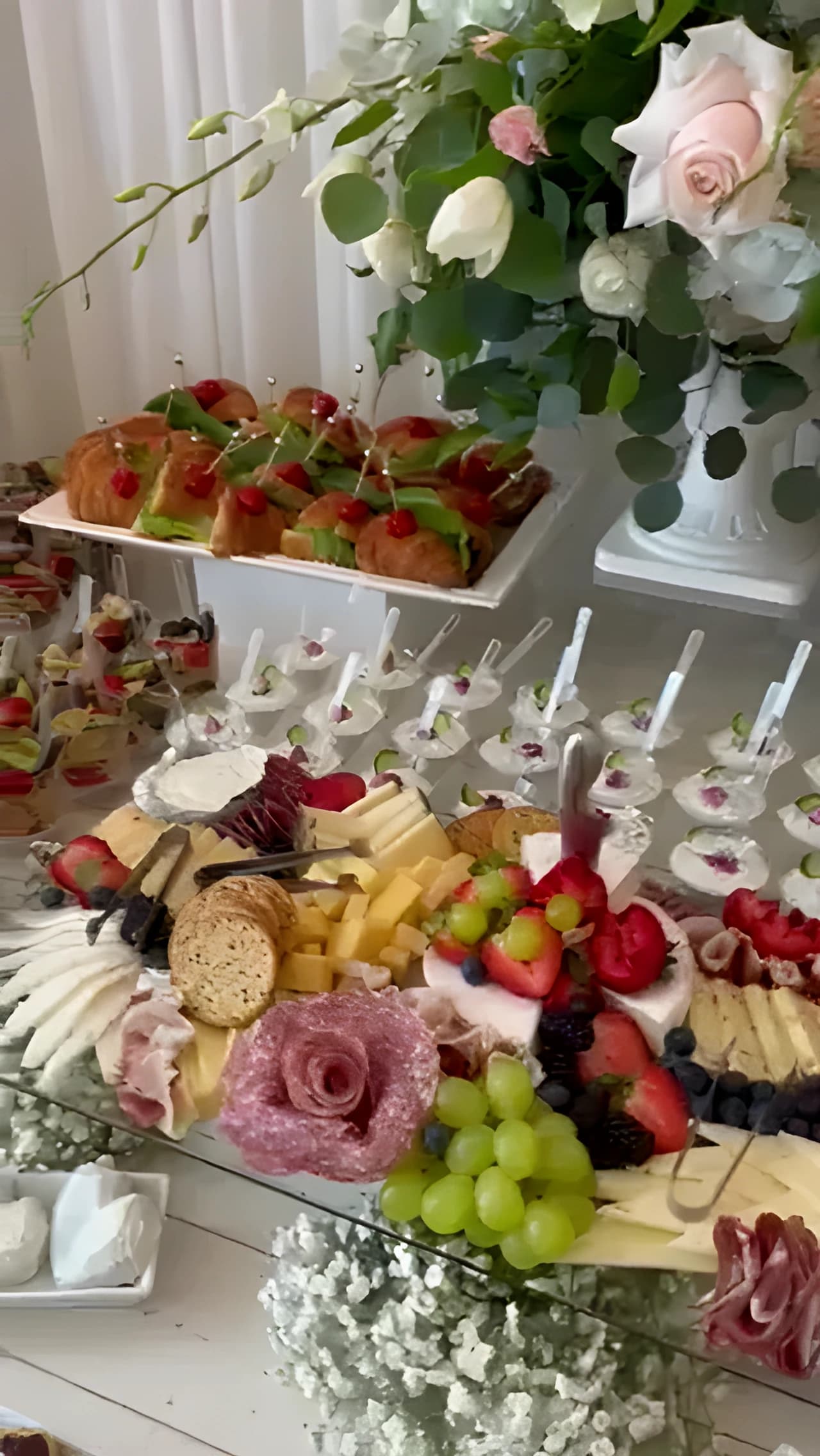 Mirror-top grazing table with cheeses, cured meats, fruit, desserts, and pink-and-white flowers