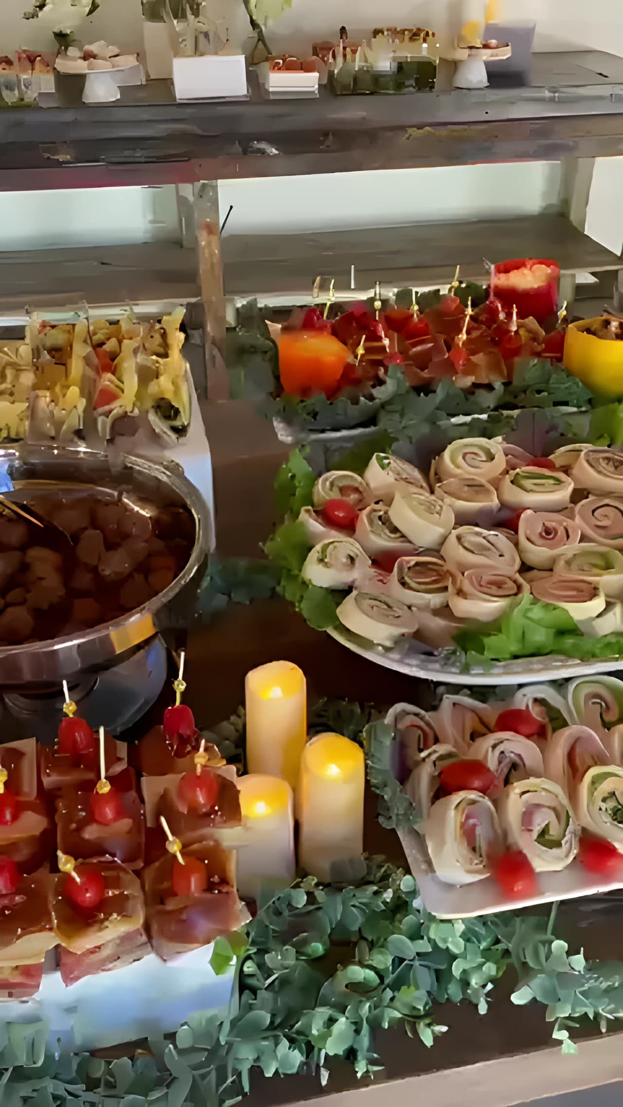 Appetizer table with pinwheels, Caprese skewers, meatballs, greenery, and flameless candles