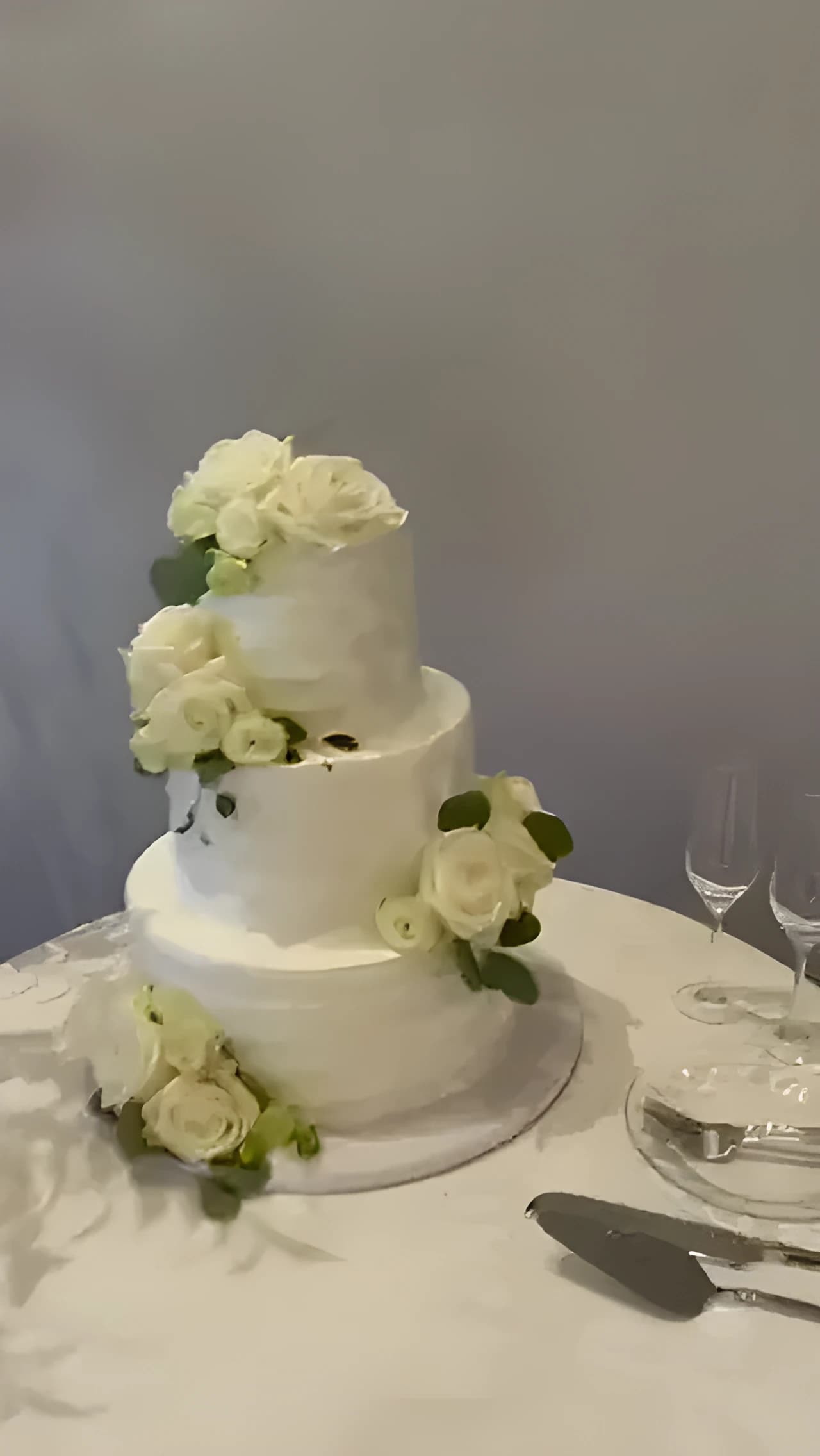 Three-tier white wedding cake with white roses on a white linen table