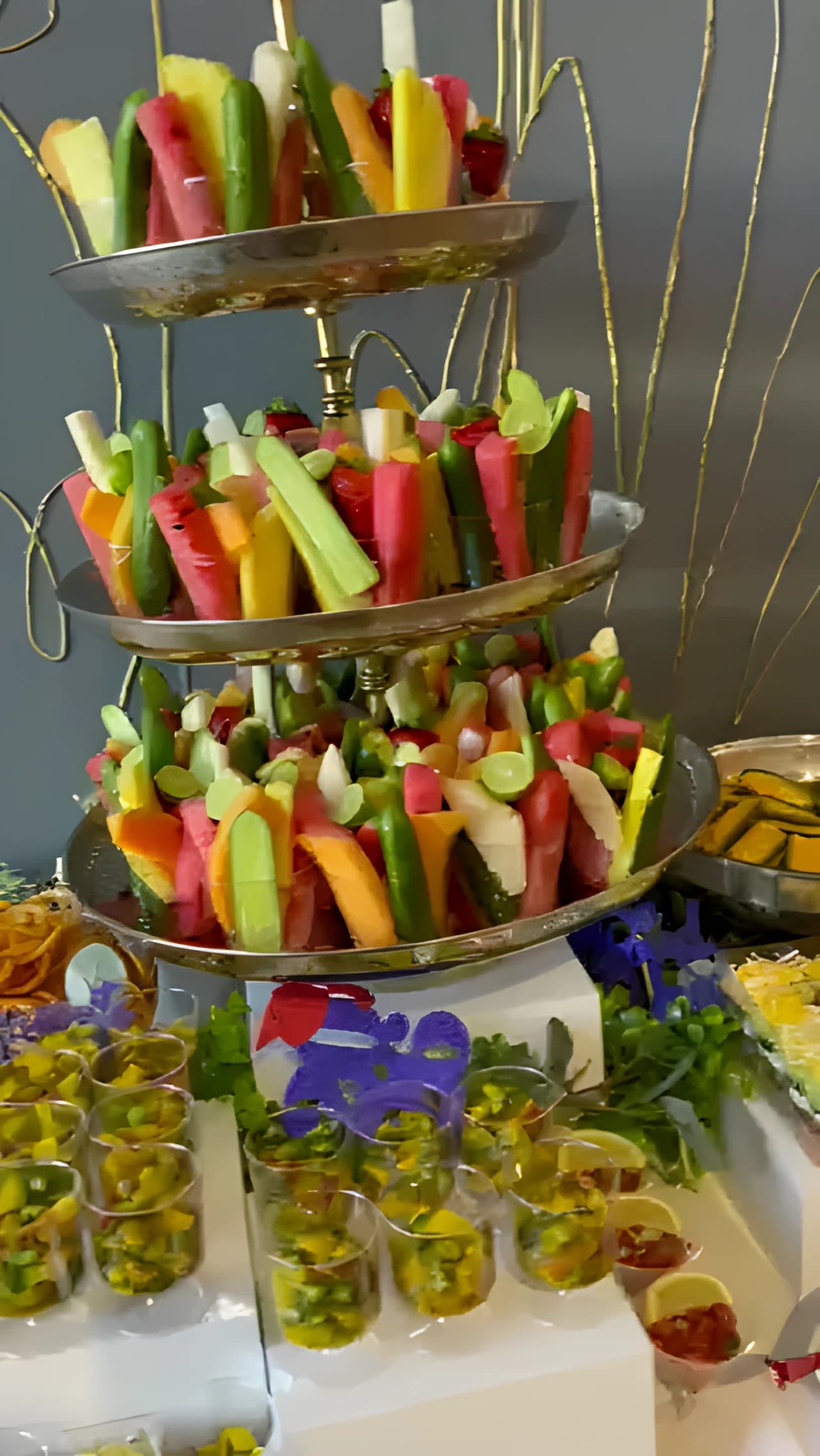 Tiered display of watermelon, cucumber, and other cut produce above appetizer cups