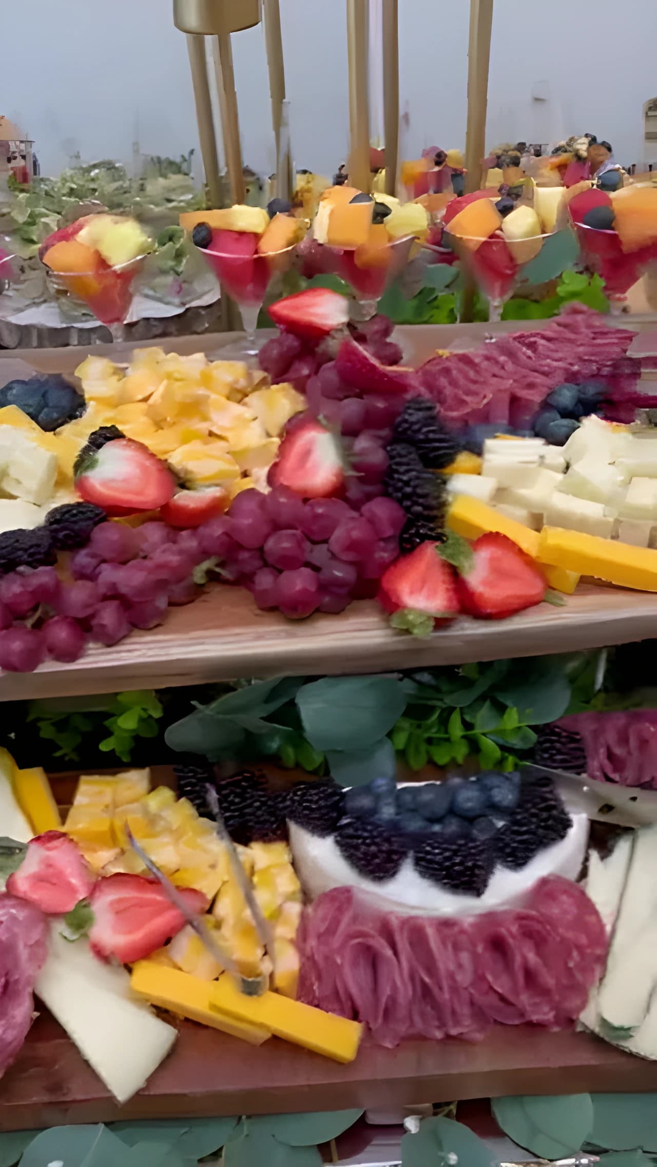 Two raised grazing boards with cheeses, cured meats, berries, grapes, and fruit cups