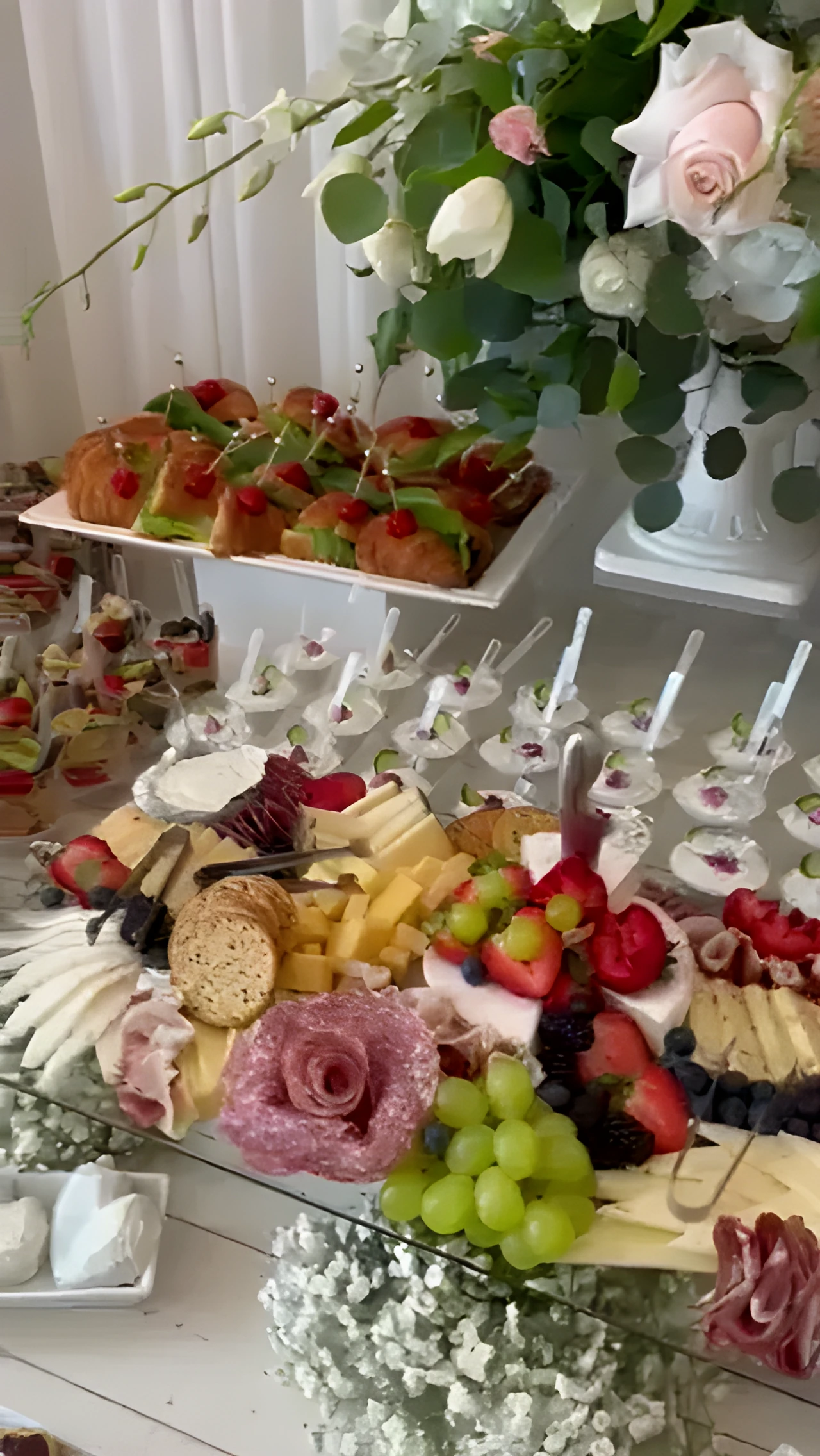 Mirror-top grazing table with cheeses, cured meats, fruit, desserts, and pink-and-white flowers