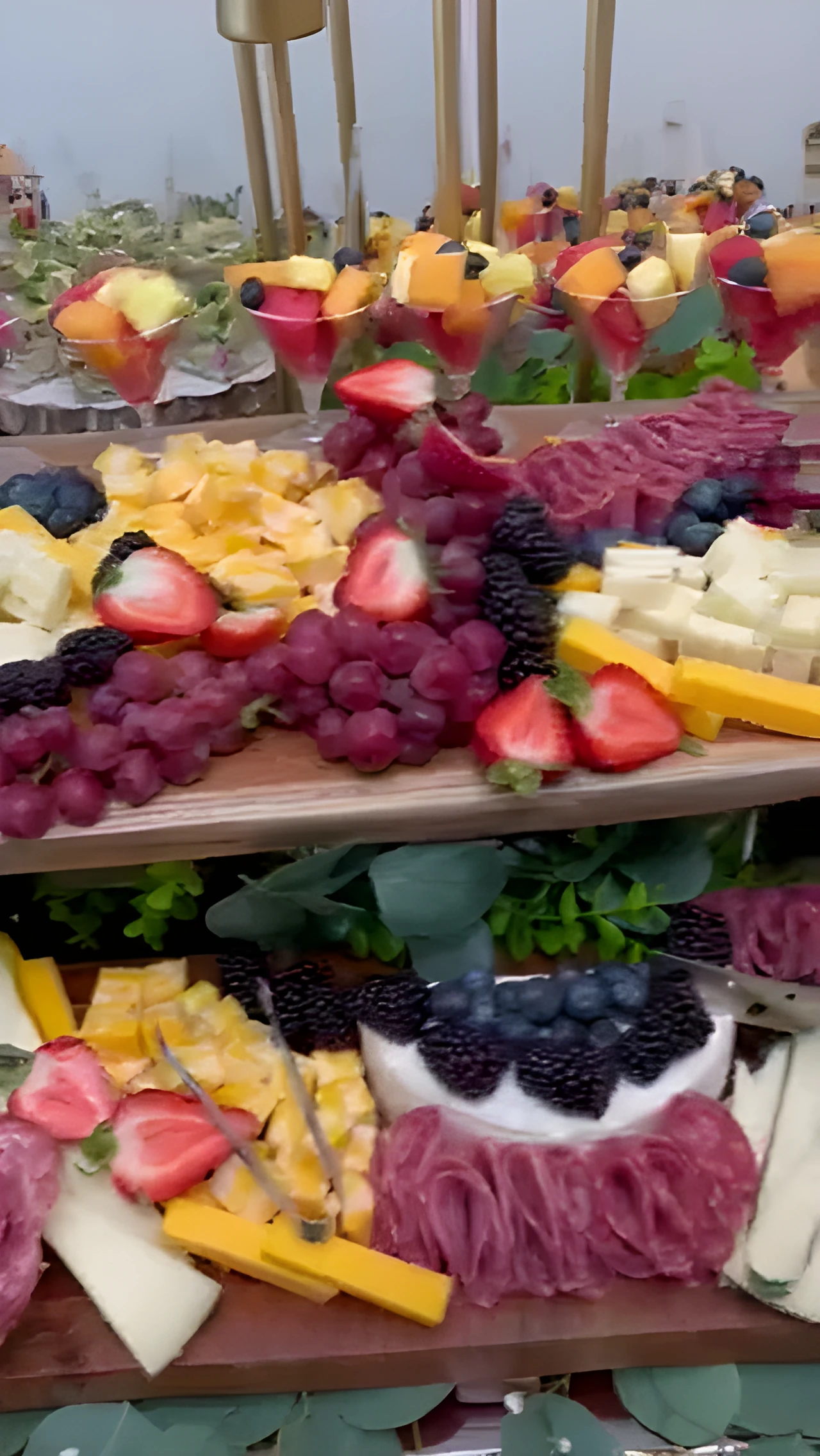 Two raised grazing boards with cheeses, cured meats, berries, grapes, and fruit cups